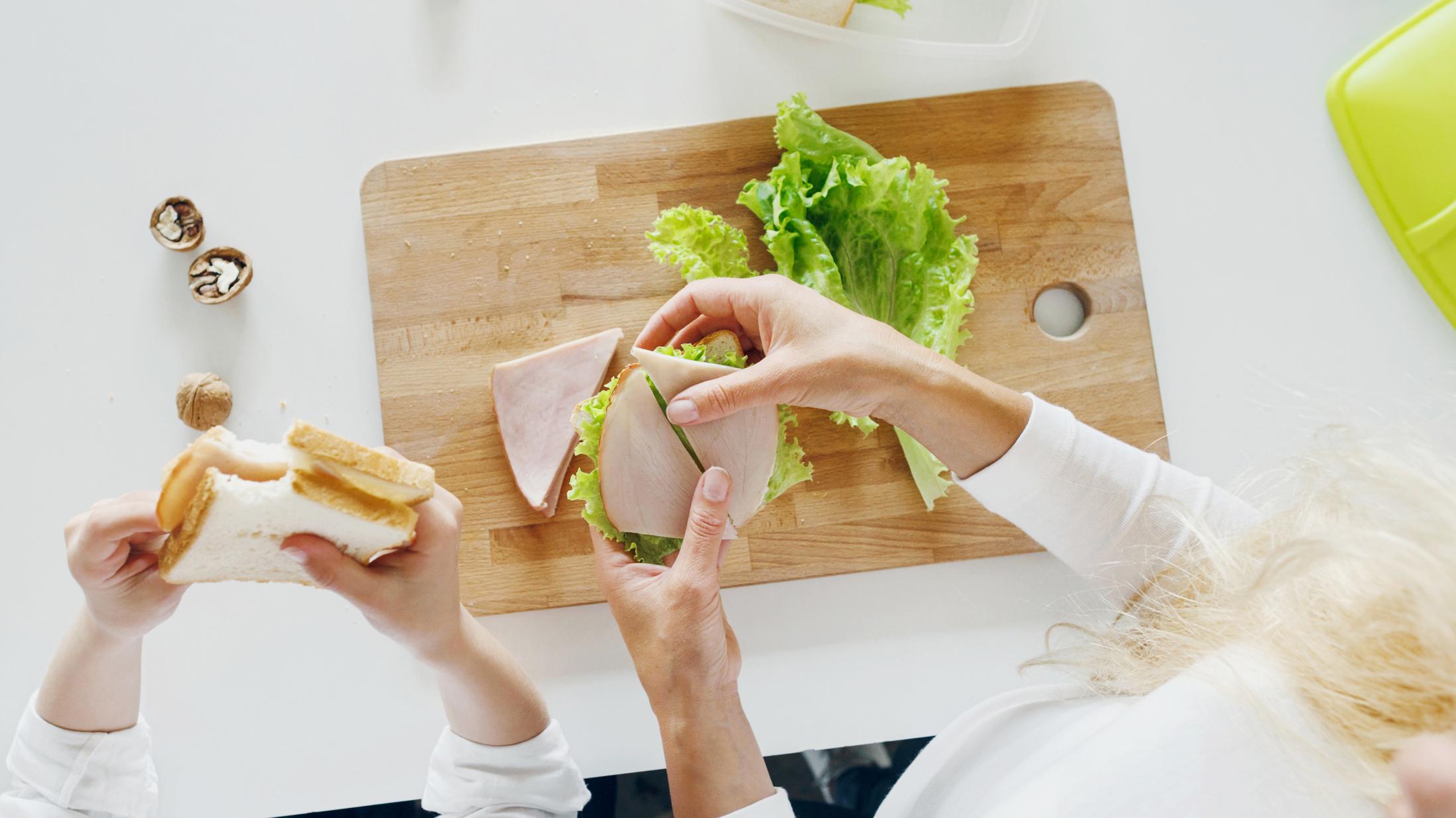 Des mains préparent un sandwich alors qu'une autre paire de mains tiennent un sandwich entamé